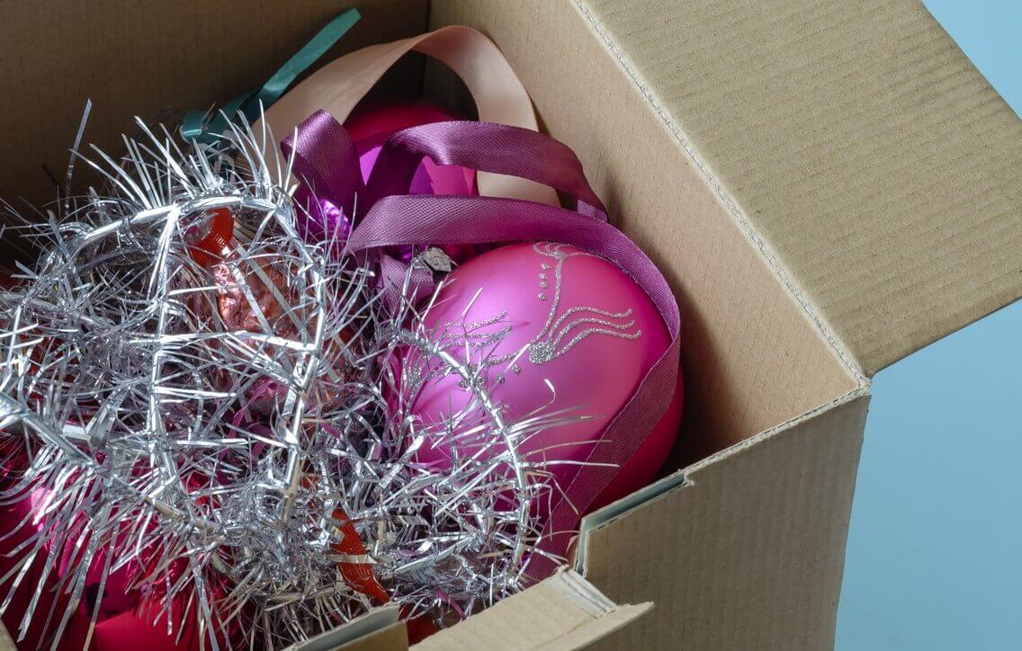 A cardboard box filled with Christmas decorations against a blue background. 