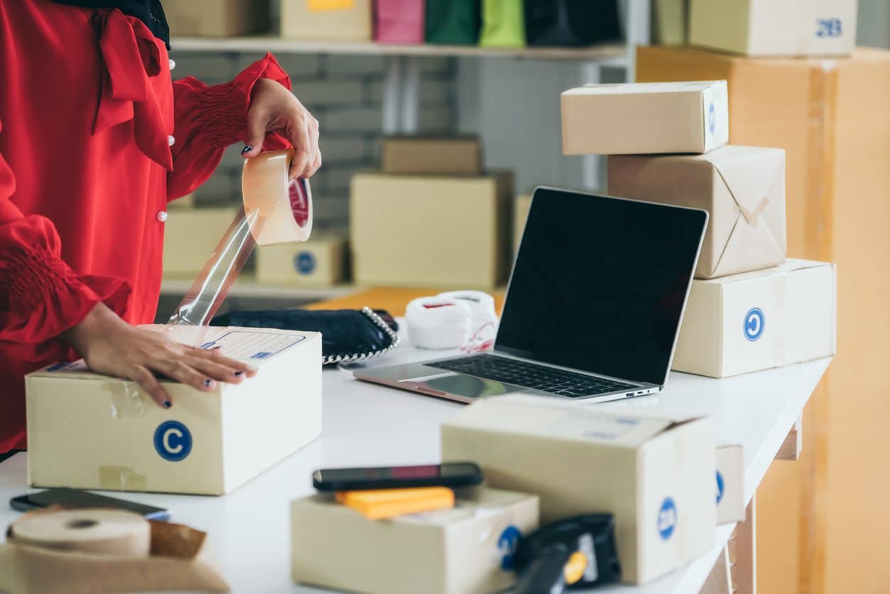 A woman packing boxes in front of a laptop on a white table