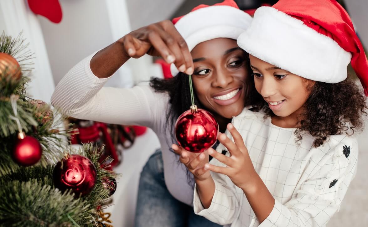 A woman and child decorating their Christmas tree together with red ornaments.